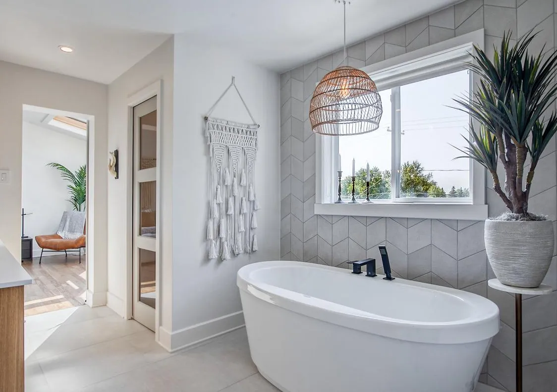 Salle de bain lumineuse avec baignoire autoportante, mur en tuiles chevron et suspension en rotin