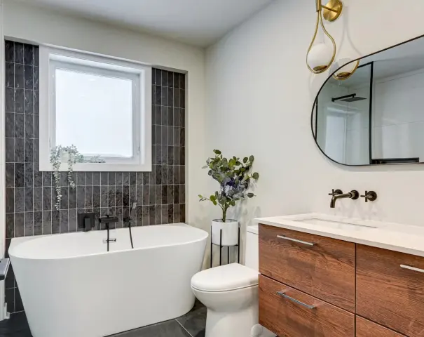Salle de bain avec baignoire, vanité de bois et mur de tuiles foncées